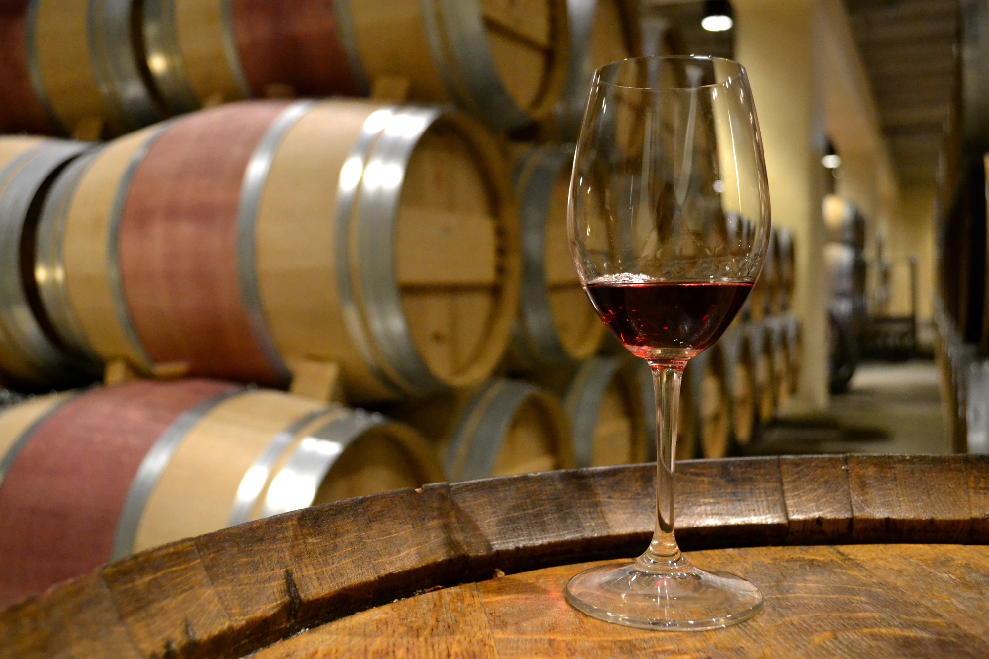 Glass of red wine sitting on a wine barrel in a wine cellar during a tour and tasting in Napa Valley